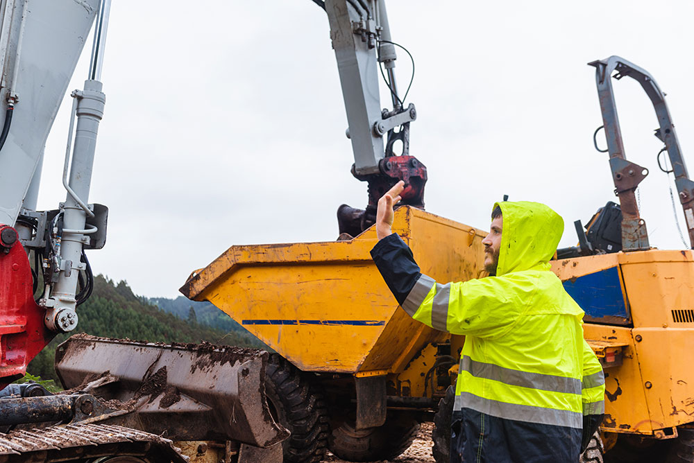 Construction worker guides an excavator operator